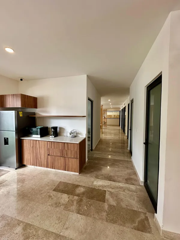 A vibrant rooftop pool bar at TownCenter Zama, featuring a sparkling blue swimming pool, a bar counter with four wooden stools, and modern pendant lights, all set against a clear blue sky with lush green foliage in the background, showcasing a rea...