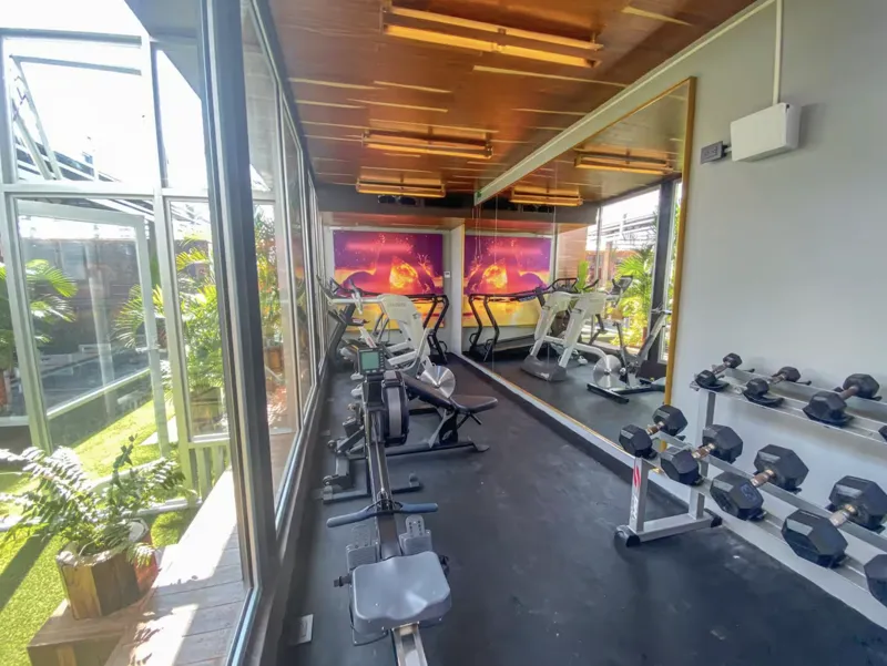 Aerial view of Residencia Condos in Playa del Carmen, featuring a large, completed rooftop infinity pool with people swimming, surrounded by lounge areas and lush greenery, with the Caribbean Sea visible in the background under a partly cloudy sky.
