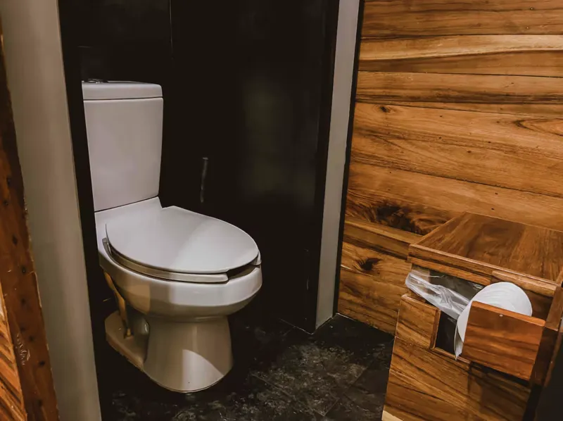 Aerial view of Residencia Condos in Playa del Carmen, featuring a large, completed rooftop infinity pool with people swimming, surrounded by lounge areas and lush greenery, with the Caribbean Sea visible in the background under a partly cloudy sky.