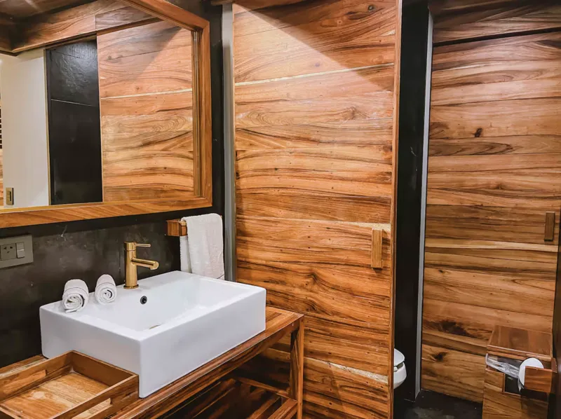 Aerial view of Residencia Condos in Playa del Carmen, featuring a large, completed rooftop infinity pool with people swimming, surrounded by lounge areas and lush greenery, with the Caribbean Sea visible in the background under a partly cloudy sky.