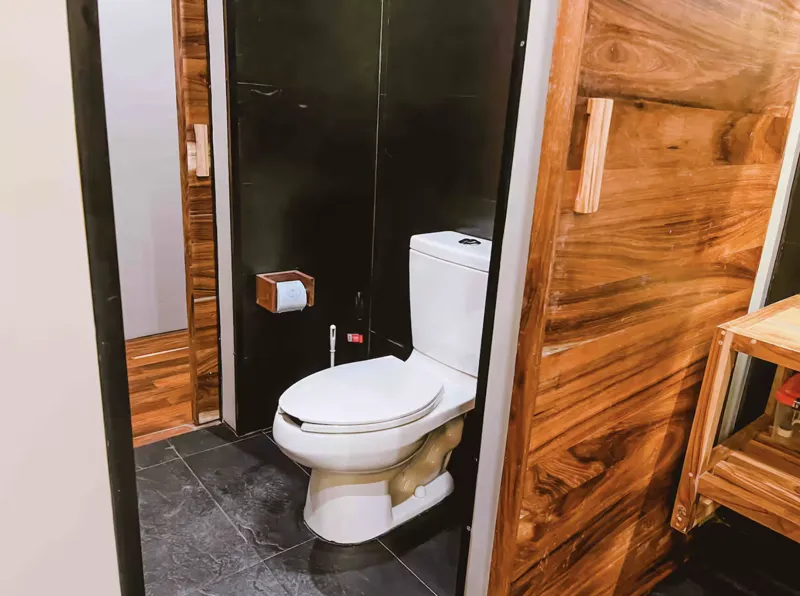 Aerial view of Residencia Condos in Playa del Carmen, featuring a large, completed rooftop infinity pool with people swimming, surrounded by lounge areas and lush greenery, with the Caribbean Sea visible in the background under a partly cloudy sky.