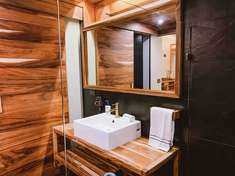 Aerial view of Residencia Condos in Playa del Carmen, featuring a large, completed rooftop infinity pool with people swimming, surrounded by lounge areas and lush greenery, with the Caribbean Sea visible in the background under a partly cloudy sky.