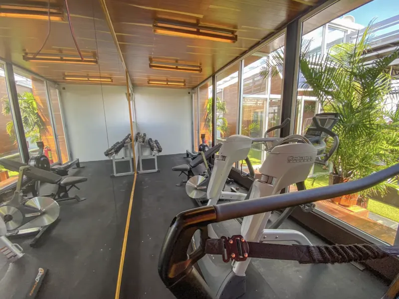 Aerial view of Residencia Condos in Playa del Carmen, featuring a large, completed rooftop infinity pool with people swimming, surrounded by lounge areas and lush greenery, with the Caribbean Sea visible in the background under a partly cloudy sky.