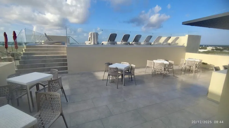 A wide shot of the sparkling rooftop infinity pool at Quartier 75, surrounded by modern lounge chairs and offering panoramic views of the city under a partly cloudy sky.