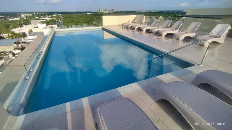 A wide shot of the sparkling rooftop infinity pool at Quartier 75, surrounded by modern lounge chairs and offering panoramic views of the city under a partly cloudy sky.