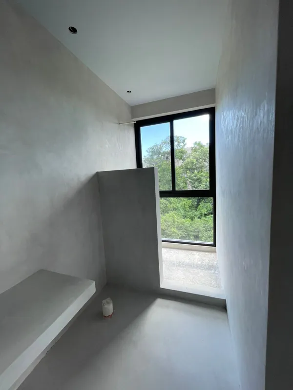 Exterior view of the Xexen y Xakah development showing significant construction progress, with scaffolding in front of the main entrance, stone cladding on the facade, and a pickup truck parked on the gravel driveway under a clear blue sky.