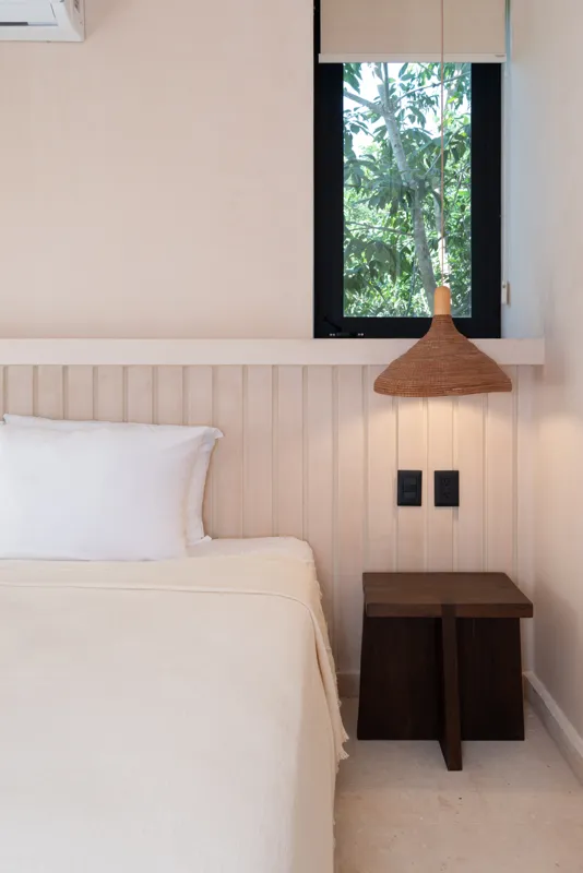 A bright, sunny rooftop terrace featuring a private swimming pool with clear blue water, surrounded by lush green plants and a light-colored building facade. A shaded pergola covers an outdoor counter area with wooden cabinets, all under a clear b...