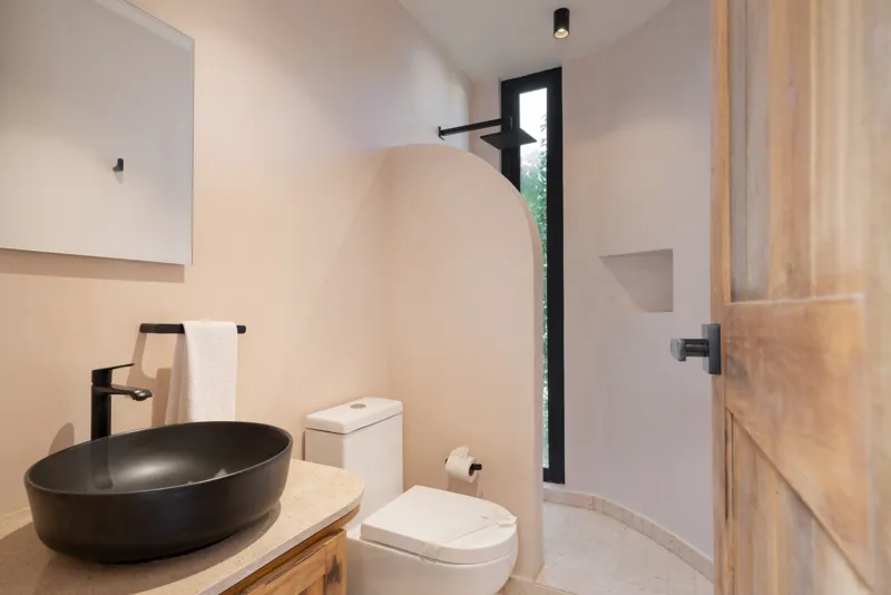 A bright, sunny rooftop terrace featuring a private swimming pool with clear blue water, surrounded by lush green plants and a light-colored building facade. A shaded pergola covers an outdoor counter area with wooden cabinets, all under a clear b...