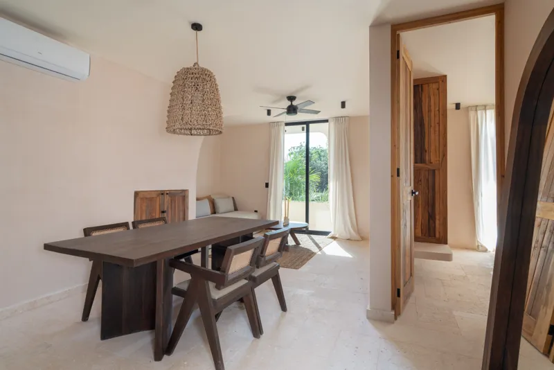 A bright, sunny rooftop terrace featuring a private swimming pool with clear blue water, surrounded by lush green plants and a light-colored building facade. A shaded pergola covers an outdoor counter area with wooden cabinets, all under a clear b...