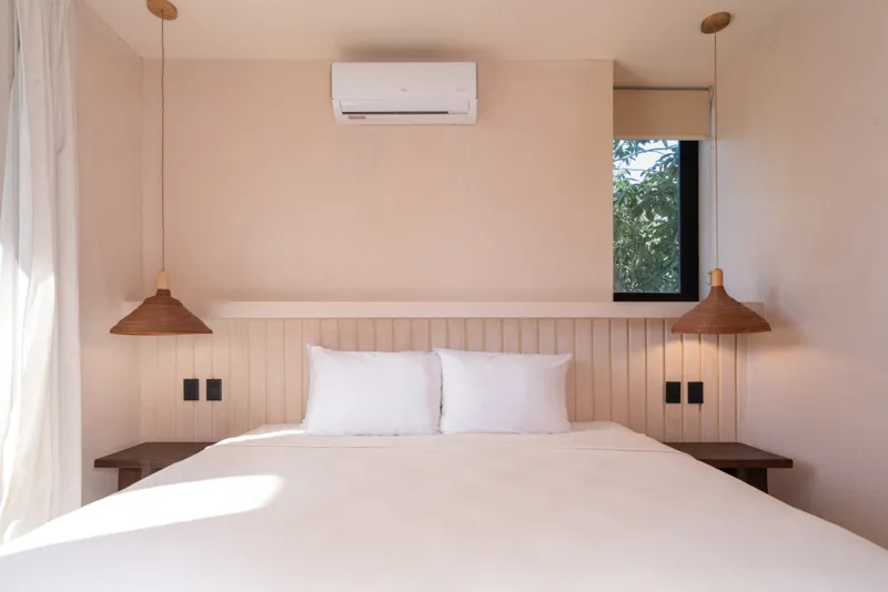 A bright, sunny rooftop terrace featuring a private swimming pool with clear blue water, surrounded by lush green plants and a light-colored building facade. A shaded pergola covers an outdoor counter area with wooden cabinets, all under a clear b...