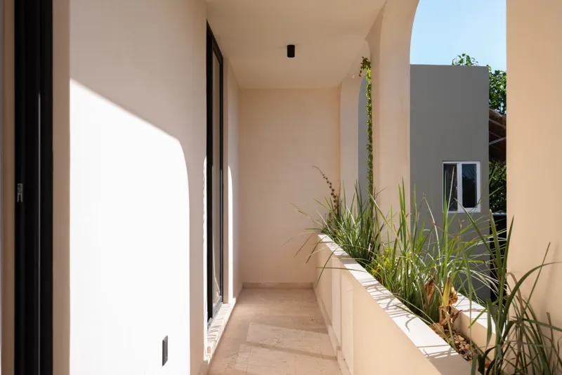 A bright, sunny rooftop terrace featuring a private swimming pool with clear blue water, surrounded by lush green plants and a light-colored building facade. A shaded pergola covers an outdoor counter area with wooden cabinets, all under a clear b...