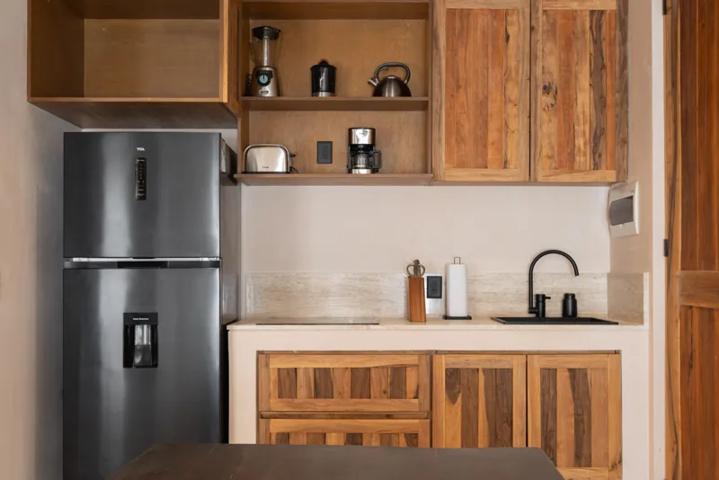 A bright, sunny rooftop terrace featuring a private swimming pool with clear blue water, surrounded by lush green plants and a light-colored building facade. A shaded pergola covers an outdoor counter area with wooden cabinets, all under a clear b...