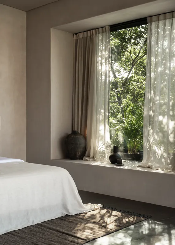 An expansive outdoor lounge area at La Reserva Tulum, featuring dark walls, built-in seating with plush cushions, natural tree trunks integrated into the design, woven pendant lights, large decorative vases, and a green patterned rug, all set agai...