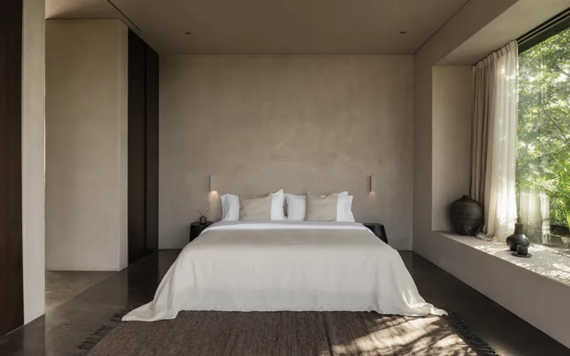 An expansive outdoor lounge area at La Reserva Tulum, featuring dark walls, built-in seating with plush cushions, natural tree trunks integrated into the design, woven pendant lights, large decorative vases, and a green patterned rug, all set agai...