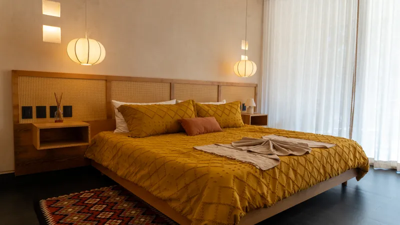 A wide shot of the open-concept dining area and kitchen in the Mestiza 15 showroom, featuring a long dark granite kitchen island with wooden bar stools, a wooden dining table set for six, modern pendant lights, and a contemporary kitchen with wood...