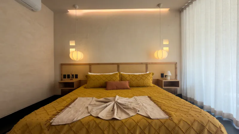 A wide shot of the open-concept dining area and kitchen in the Mestiza 15 showroom, featuring a long dark granite kitchen island with wooden bar stools, a wooden dining table set for six, modern pendant lights, and a contemporary kitchen with wood...