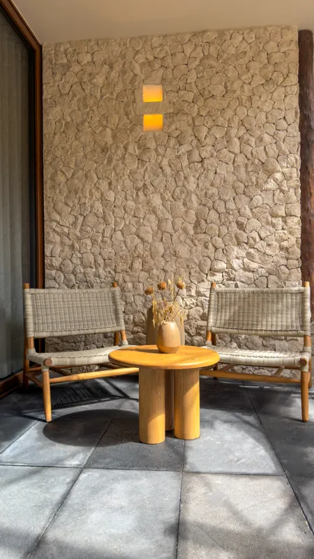 A wide shot of the open-concept dining area and kitchen in the Mestiza 15 showroom, featuring a long dark granite kitchen island with wooden bar stools, a wooden dining table set for six, modern pendant lights, and a contemporary kitchen with wood...
