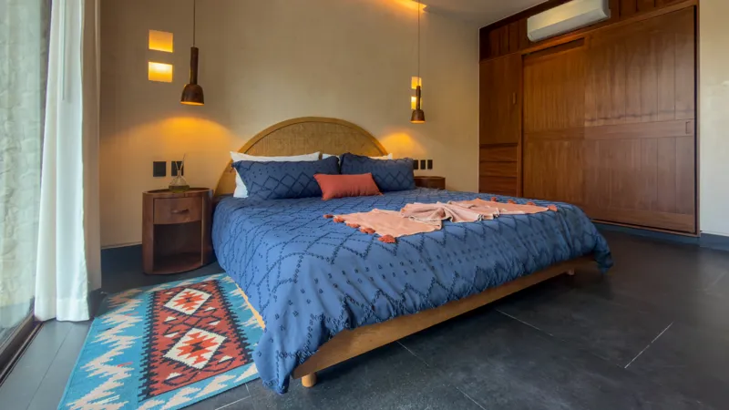 A wide shot of the open-concept dining area and kitchen in the Mestiza 15 showroom, featuring a long dark granite kitchen island with wooden bar stools, a wooden dining table set for six, modern pendant lights, and a contemporary kitchen with wood...