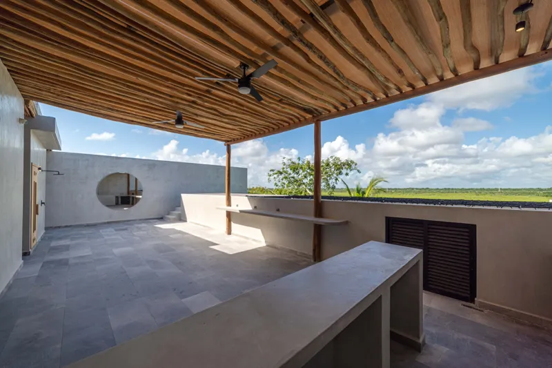 A breathtaking rooftop infinity pool at NEEA, overlooking a vibrant green jungle landscape under a bright blue sky, with a modern relaxation net area in the foreground.