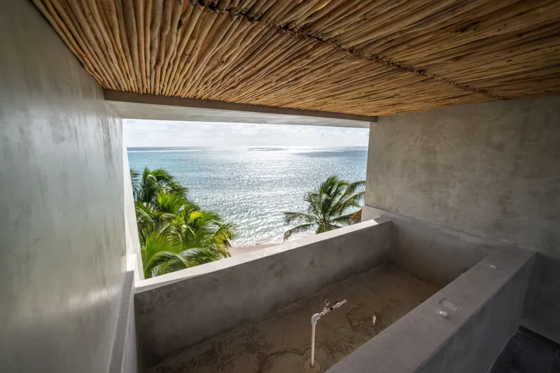 A breathtaking rooftop infinity pool at NEEA, overlooking a vibrant green jungle landscape under a bright blue sky, with a modern relaxation net area in the foreground.
