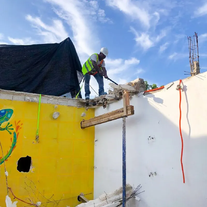 An aerial view of a demolished interior space, filled with rubble, broken concrete, and rebar, with remnants of colorful murals on the remaining walls, indicating active site preparation for the Belehu development.