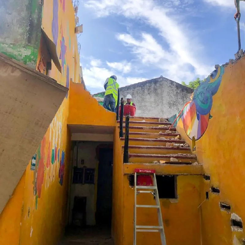 An aerial view of a demolished interior space, filled with rubble, broken concrete, and rebar, with remnants of colorful murals on the remaining walls, indicating active site preparation for the Belehu development.