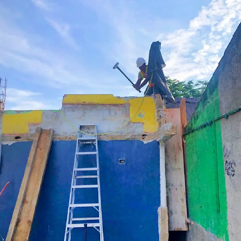 An aerial view of a demolished interior space, filled with rubble, broken concrete, and rebar, with remnants of colorful murals on the remaining walls, indicating active site preparation for the Belehu development.