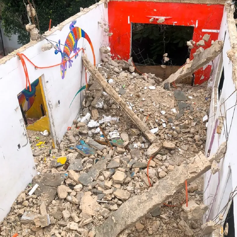 An aerial view of a demolished interior space, filled with rubble, broken concrete, and rebar, with remnants of colorful murals on the remaining walls, indicating active site preparation for the Belehu development.