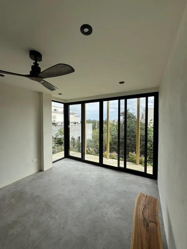 A wide shot of a finished modern apartment interior at Gold Garden, featuring a compact kitchen with concrete countertops, wooden cabinets, and a stainless steel refrigerator, opening into a living area with concrete floors, white walls, and large...