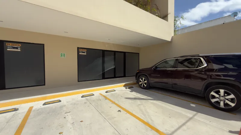 Interior view of a Studio34 apartment unit under construction, showing bare concrete block walls, an unfinished concrete floor, exposed electrical conduits on the ceiling, and a partially installed wooden door frame leading to another room. Red ma...