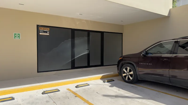 Interior view of a Studio34 apartment unit under construction, showing bare concrete block walls, an unfinished concrete floor, exposed electrical conduits on the ceiling, and a partially installed wooden door frame leading to another room. Red ma...