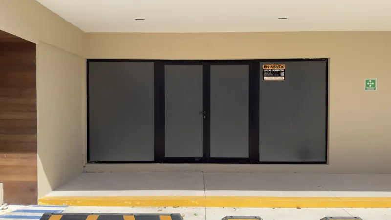 A full exterior view of the Studio34 development, a six-story modern building with a beige facade, dark vertical accents, and balconies, appearing largely complete under a clear blue sky. Orange traffic cones are visible on the street in front, an...