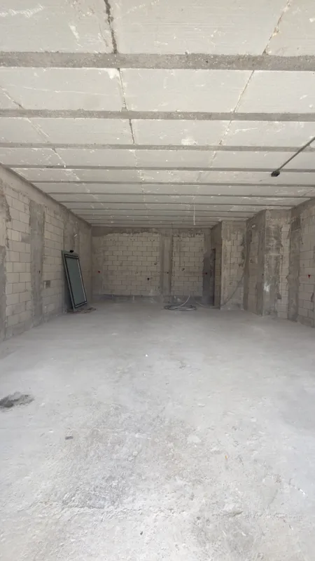 A full exterior view of the Studio34 development, a six-story modern building with a beige facade, dark vertical accents, and balconies, appearing largely complete under a clear blue sky. Orange traffic cones are visible on the street in front, an...