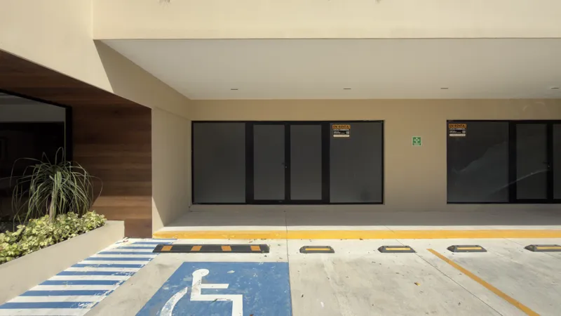 A full exterior view of the Studio34 development, a six-story modern building with a beige facade, dark vertical accents, and balconies, appearing largely complete under a clear blue sky. Orange traffic cones are visible on the street in front, an...