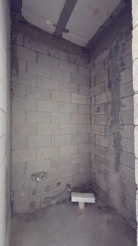 A full exterior view of the Studio34 development, a six-story modern building with a beige facade, dark vertical accents, and balconies, appearing largely complete under a clear blue sky. Orange traffic cones are visible on the street in front, an...