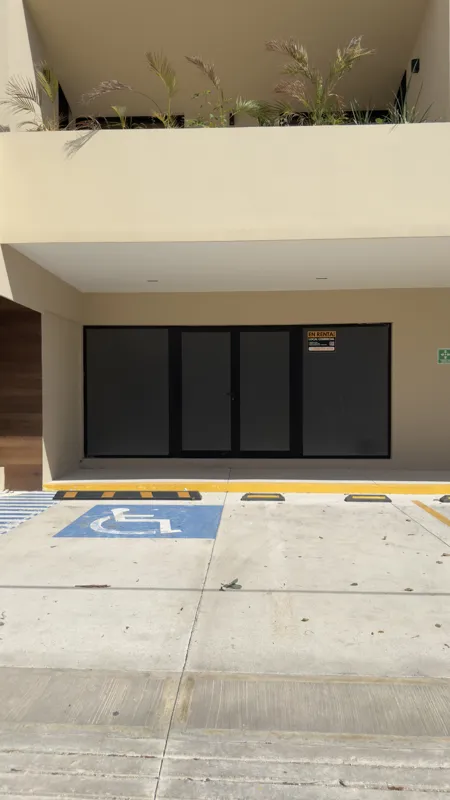 A full exterior view of the Studio34 development, a six-story modern building with a beige facade, dark vertical accents, and balconies, appearing largely complete under a clear blue sky. Orange traffic cones are visible on the street in front, an...