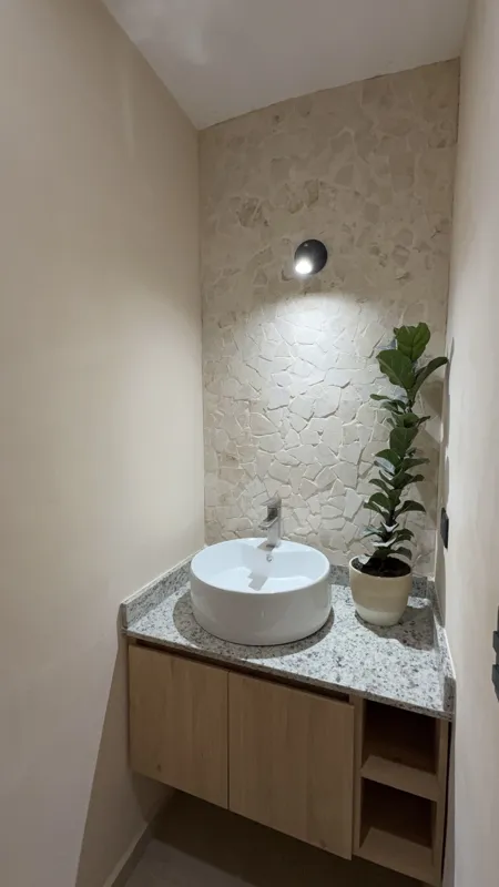 A wide shot of a modern, fully furnished kitchen and dining area in a Gobernador 28 showroom unit, featuring light wood cabinetry, a granite breakfast bar with stools, a wooden dining table with chairs, decorative woven pendant lights, and white m...