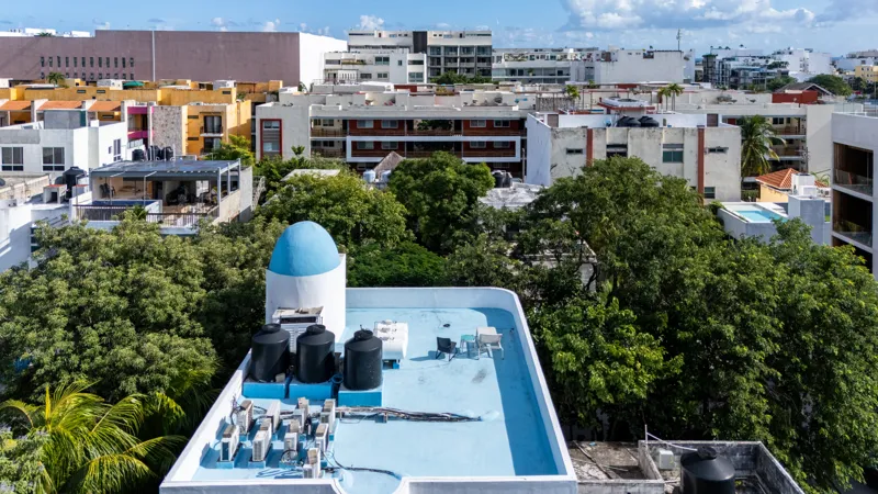 A bright and inviting living room in Casa Dragonfly featuring a white sectional sofa with colorful Moroccan-inspired pillows, a wooden coffee table with a decorative lantern, a round patterned floor cushion, and a large ornate window, showcasing t...