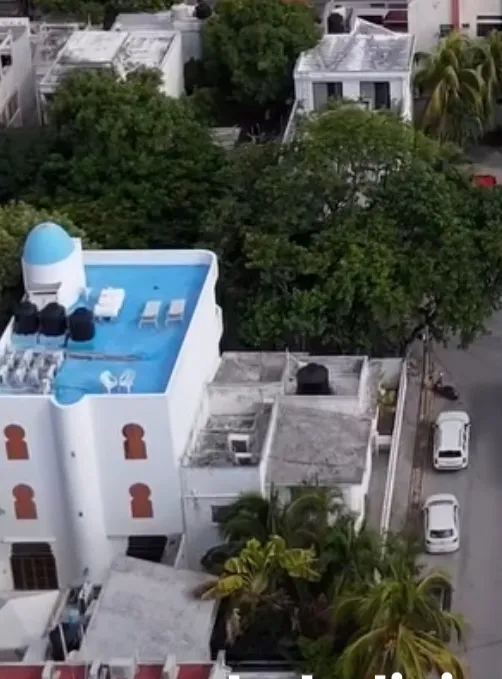 A bright and inviting living room in Casa Dragonfly featuring a white sectional sofa with colorful Moroccan-inspired pillows, a wooden coffee table with a decorative lantern, a round patterned floor cushion, and a large ornate window, showcasing t...
