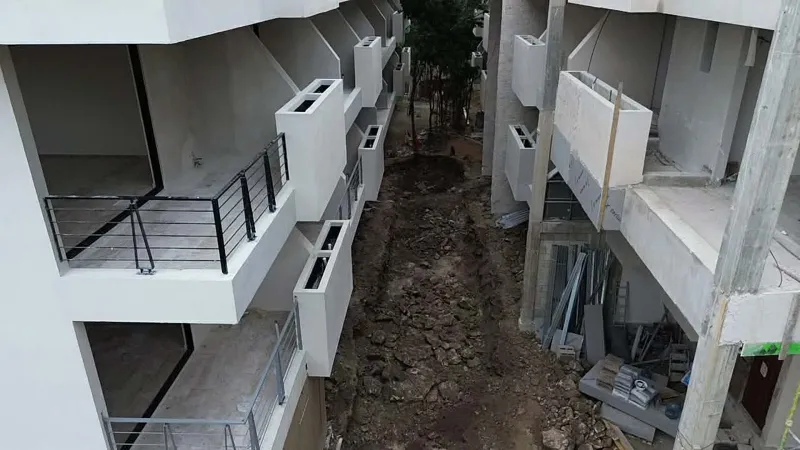 Aerial view of the Zamajal development in Tulum, showcasing multiple buildings in various stages of construction, with a construction vehicle on the ground and lush green jungle surrounding the site.