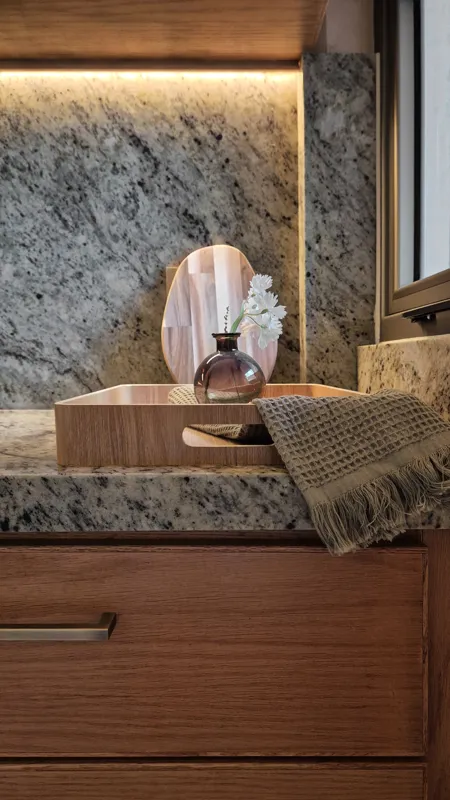 A beautifully furnished dining area with a wooden table set for four, surrounded by modern wooden chairs, leading into a contemporary kitchen with dark wood cabinets, light granite countertops, and stainless steel appliances, all under warm accent...