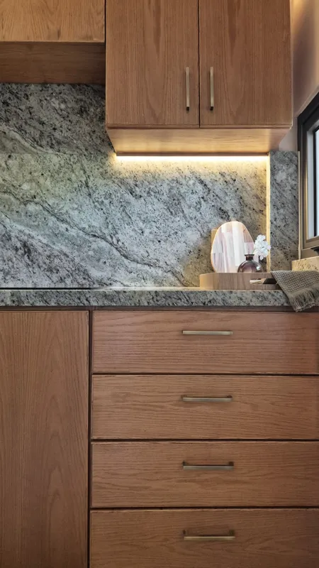 A beautifully furnished dining area with a wooden table set for four, surrounded by modern wooden chairs, leading into a contemporary kitchen with dark wood cabinets, light granite countertops, and stainless steel appliances, all under warm accent...