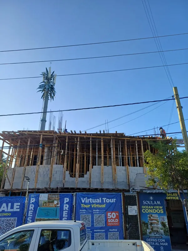 An exterior shot of the Soulam development under construction in Puerto Morelos, showing the concrete structure and scaffolding. A sign in the foreground indicates 'Virtual Tour' and '50% SOLD', with another sign for 'Soulam Ocean View Condos' and...