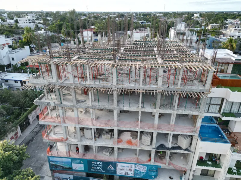 Aerial view of the Maia development showing a multi-story concrete structure under construction. The building has several completed concrete slabs, with extensive wooden formwork and rebar visible on the upper levels, particularly for the 6th floo...