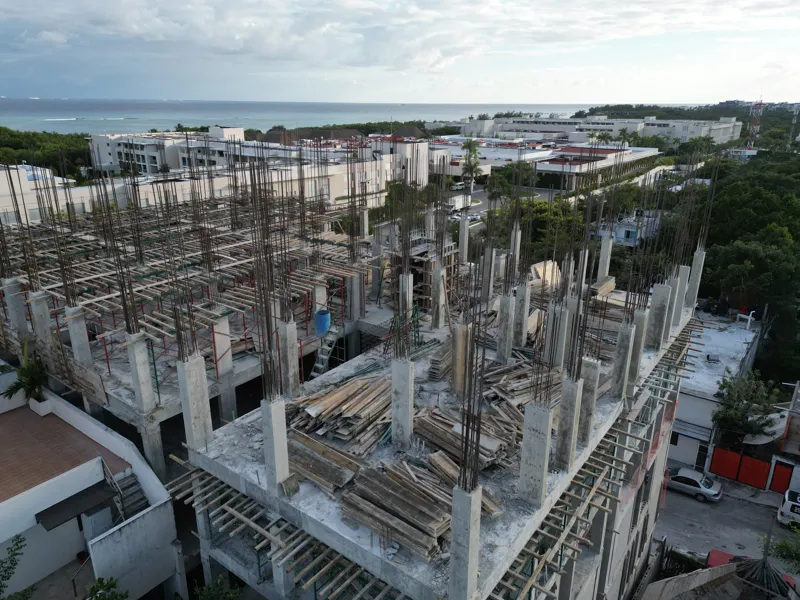 Aerial view of the Maia development showing a multi-story concrete structure under construction. The building has several completed concrete slabs, with extensive wooden formwork and rebar visible on the upper levels, particularly for the 6th floo...