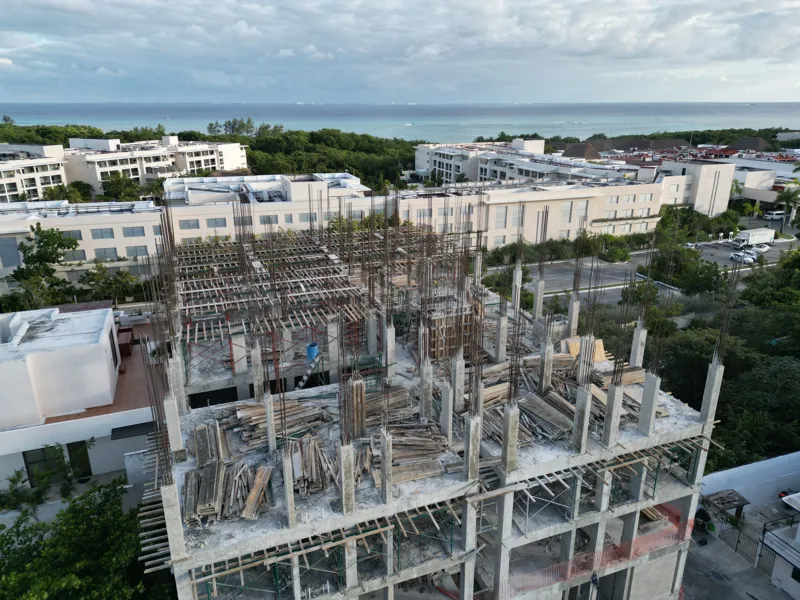 Aerial view of the Maia development showing a multi-story concrete structure under construction. The building has several completed concrete slabs, with extensive wooden formwork and rebar visible on the upper levels, particularly for the 6th floo...