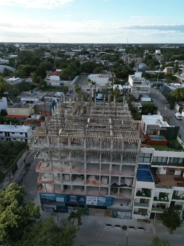 Aerial view of the Maia development showing a multi-story concrete structure under construction. The building has several completed concrete slabs, with extensive wooden formwork and rebar visible on the upper levels, particularly for the 6th floo...