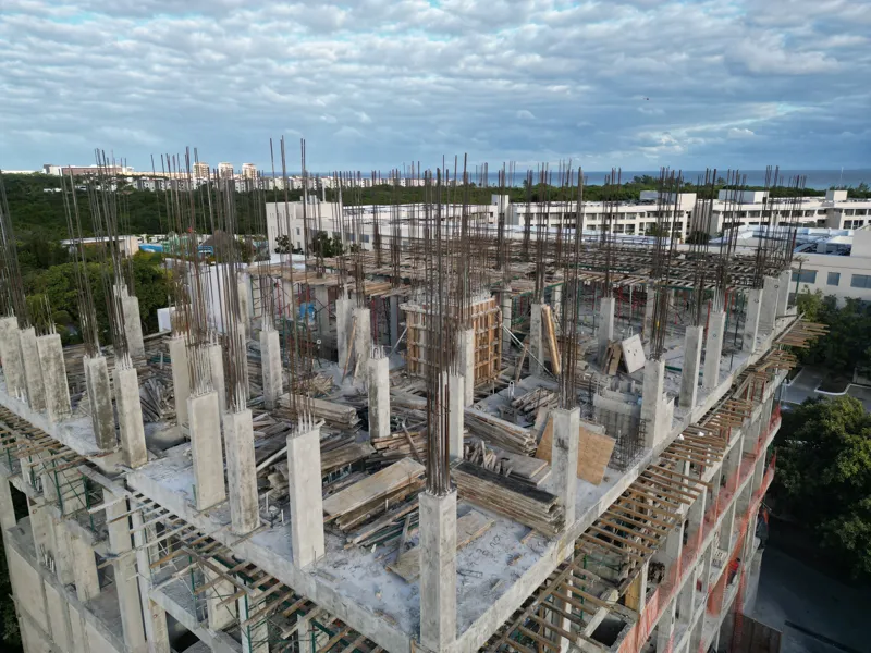 Aerial view of the Maia development showing a multi-story concrete structure under construction. The building has several completed concrete slabs, with extensive wooden formwork and rebar visible on the upper levels, particularly for the 6th floo...