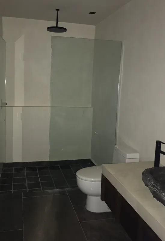A modern kitchen in a Humana residential unit, featuring dark tiled floors, dark wood and grey cabinets, a stainless steel refrigerator, an integrated oven, and a black countertop with a sink and faucet. A large window is visible on the right.