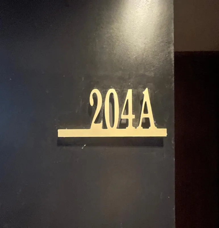A modern kitchen in a Humana residential unit, featuring dark tiled floors, dark wood and grey cabinets, a stainless steel refrigerator, an integrated oven, and a black countertop with a sink and faucet. A large window is visible on the right.